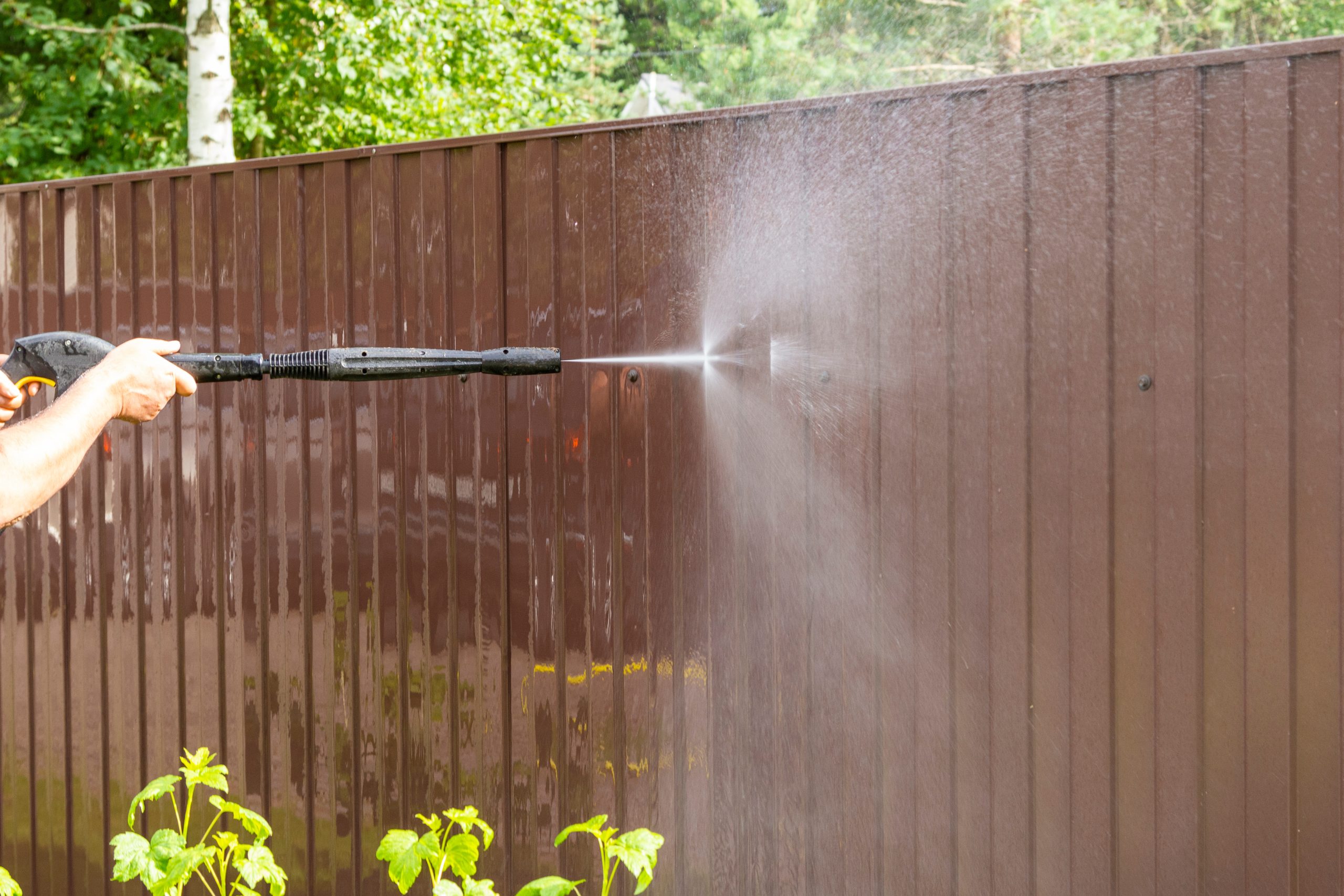 Cleaning fence with high pressure power washer, cleaning dirty wall.